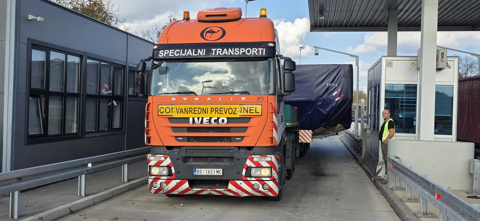 Orange IVECO Stralis with a lowboy trailer and covered oversized cargo