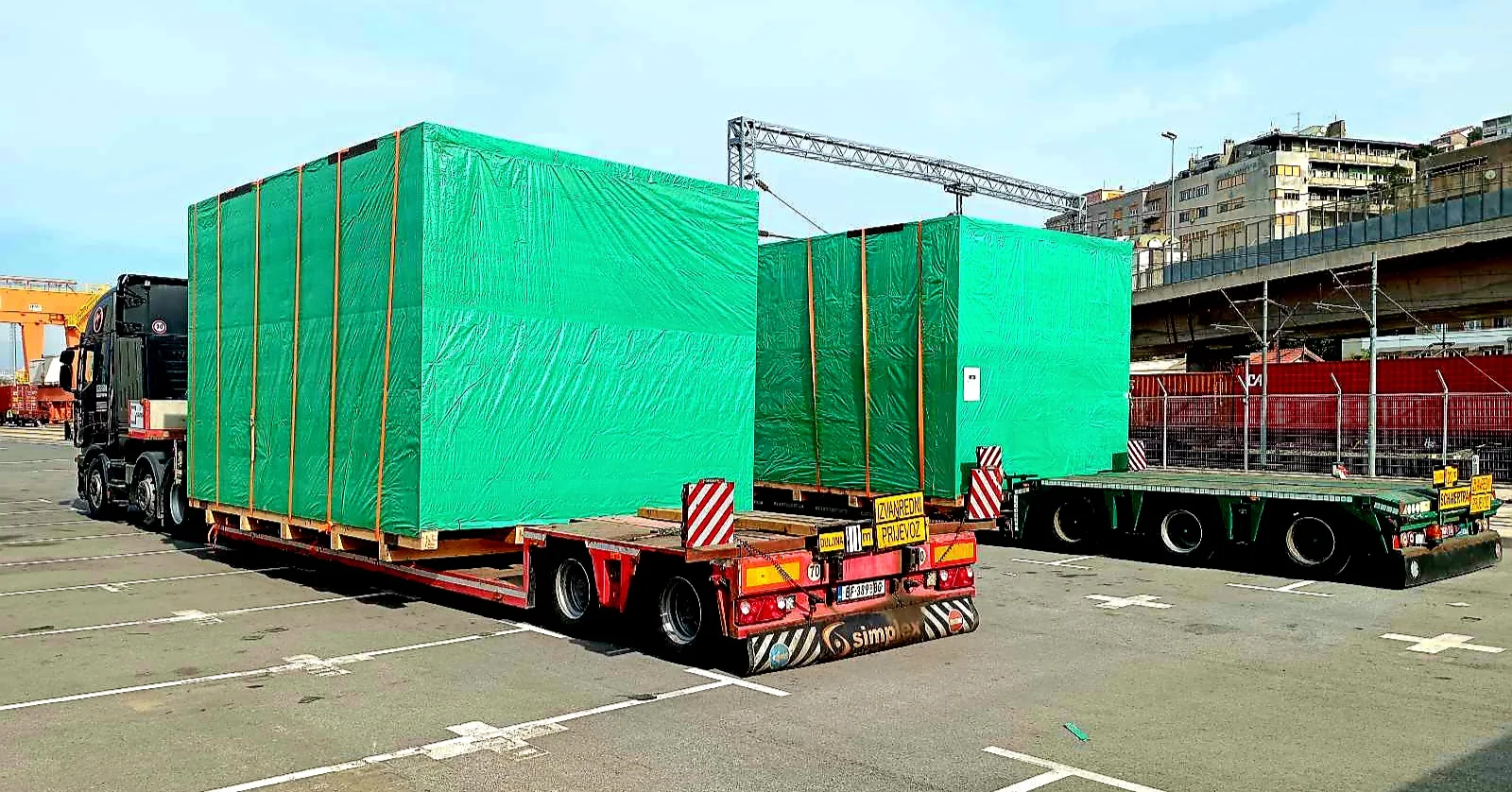 Oversized modules wrapped in green tarpaulin on a lowboy trailer