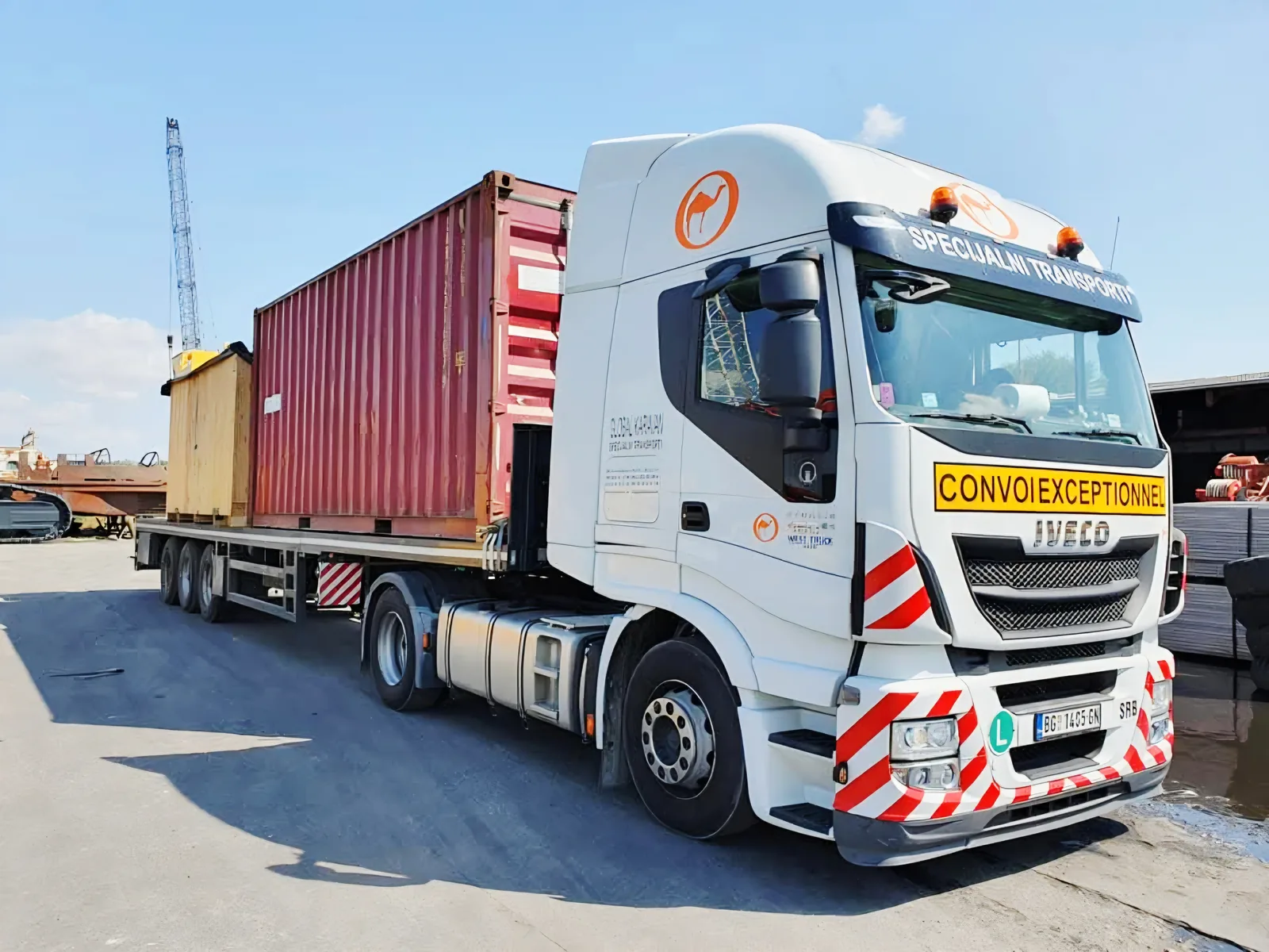 White IVECO tractor with a flatbed hauling a container and a wooden crate